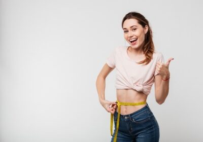 91792094-portrait-of-a-slim-satisfied-woman-holding-measuring-tape-around-her-waist-and-showing-thumbs-up-iso